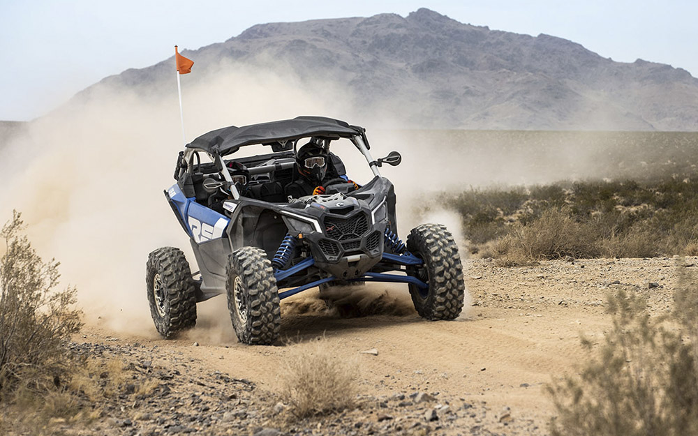 UTV azul, preto e branco acelerando em estrada de terra com montanhas ao fundo